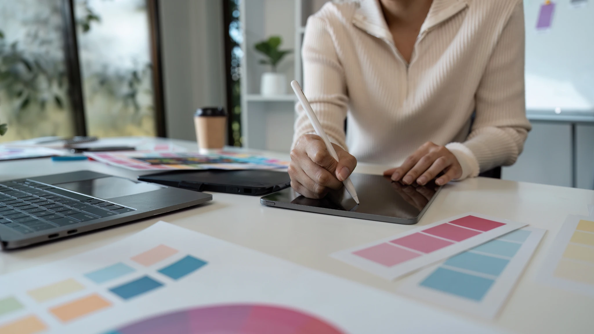 A woman is focused on a design project, surrounded by colorful swatches and sketching ideas on her workspace.