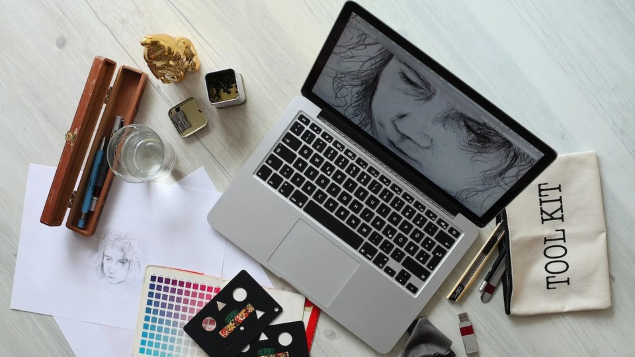 A laptop, drawing materials, and various items are neatly arranged on a wooden table.