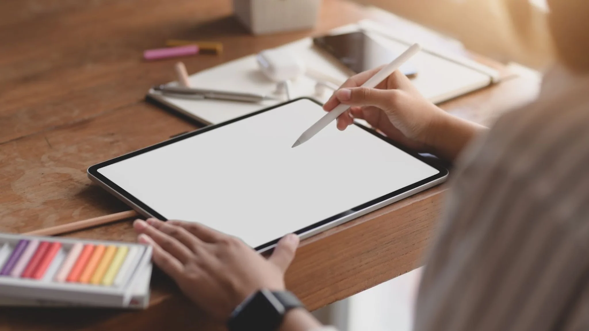 Woman using a tablet with a blank screen, resting on a wooden table, focused on her device.