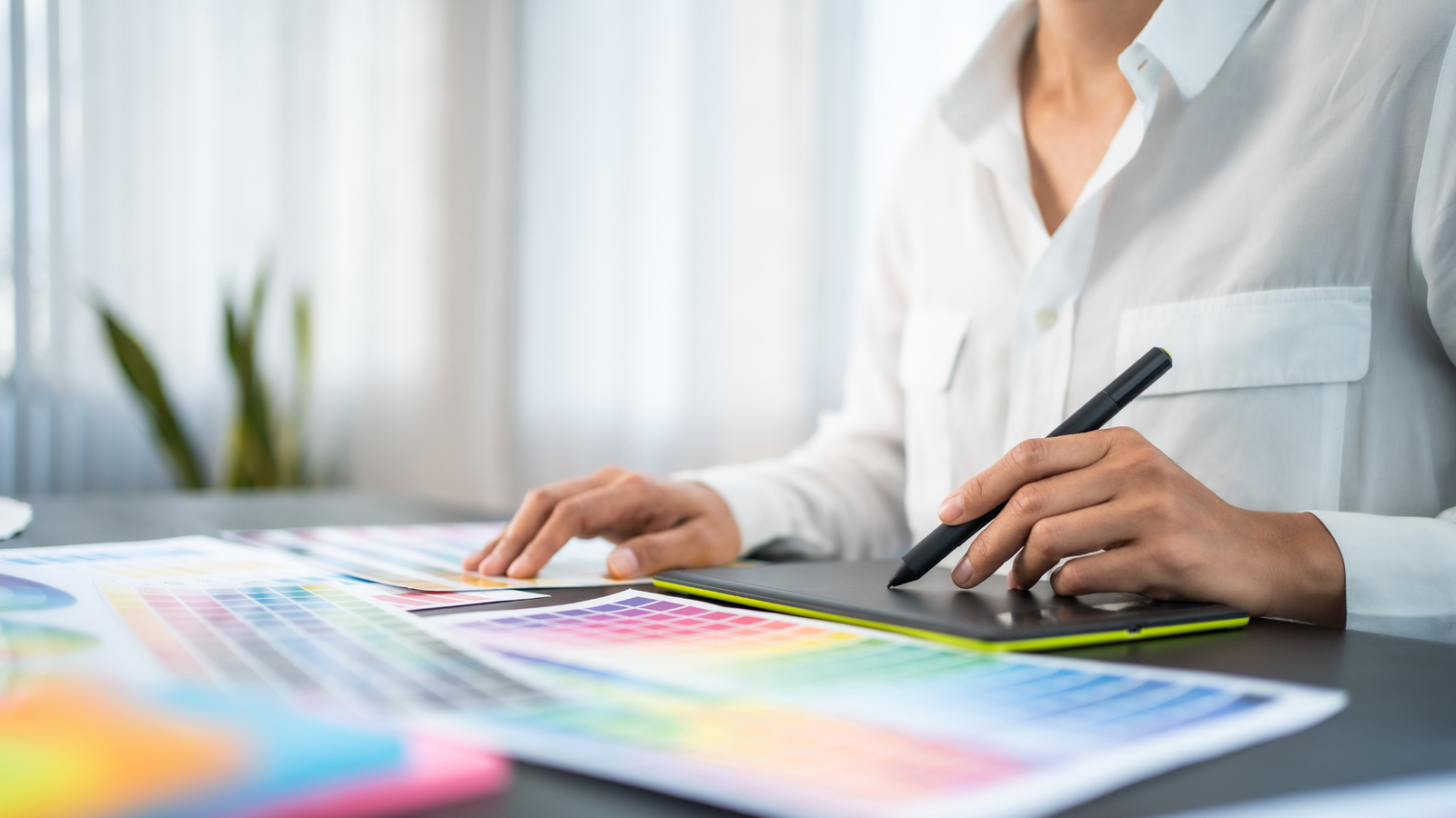 A woman focused on her design work, sketching with a pen on paper at her desk.