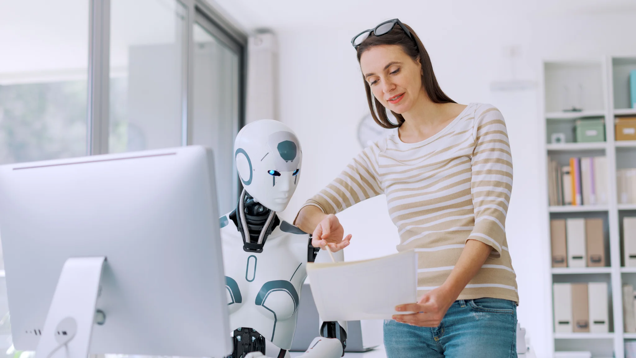 A woman stands beside a robot, holding a piece of paper and smiling, showcasing a collaborative moment.