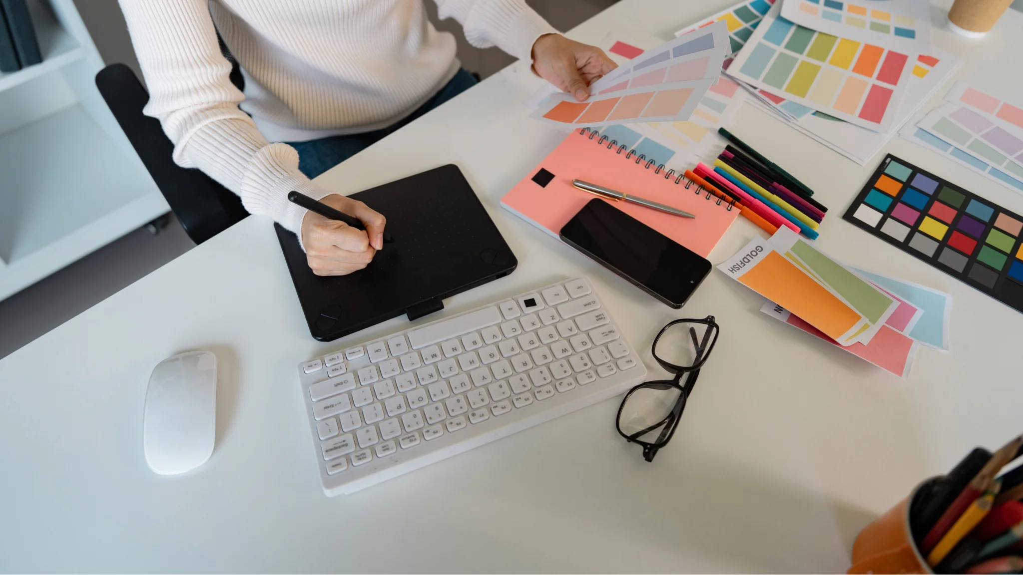 A woman sits at a desk with a computer and a pen, focused on her work.