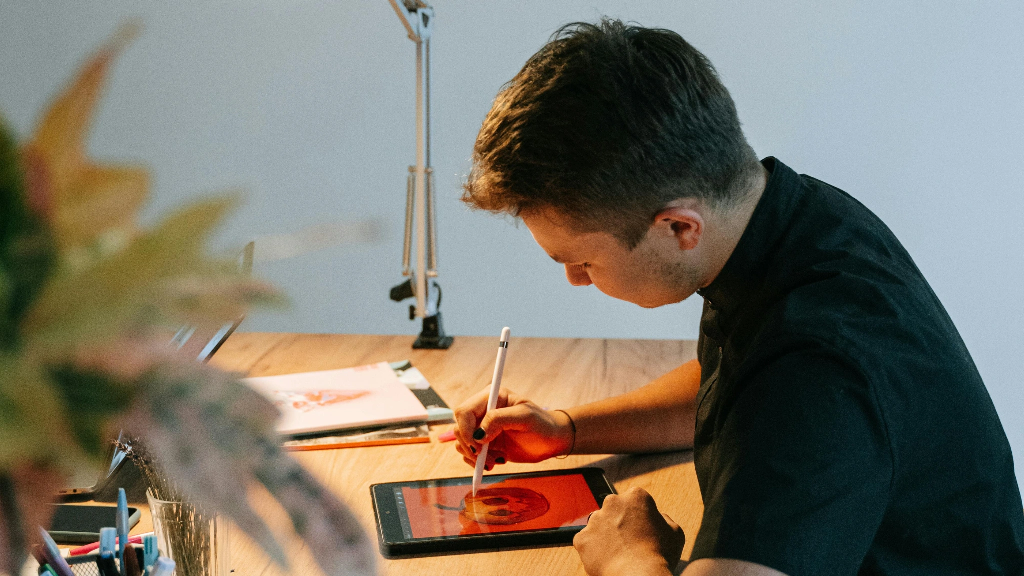 A man sits at a desk, focused on working on a tablet, surrounded by a tidy workspace.
