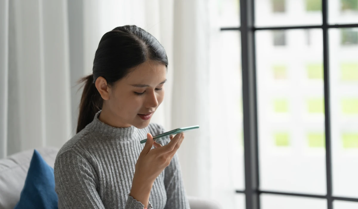 Asian woman sitting in a cozy living room, focused on her smartphone while relaxing on a sofa.