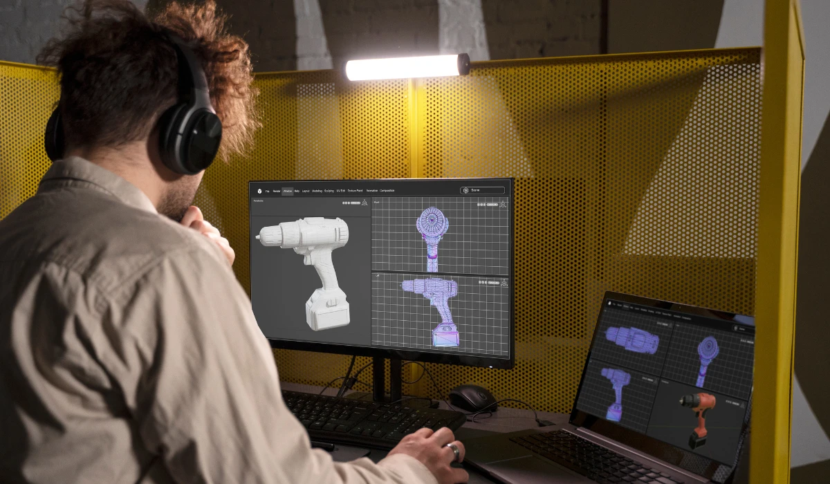 A man focused on his computer while a 3D printer operates beside him, creating a detailed object.