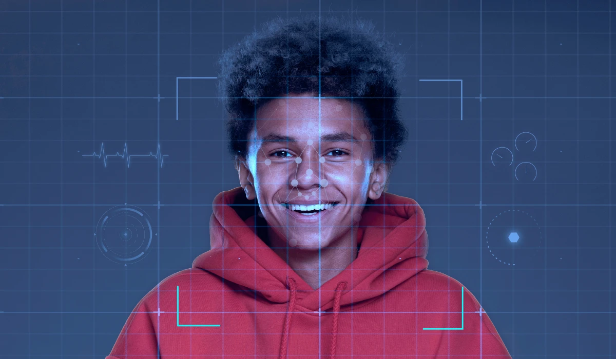 A young man wearing a red hoodie smiles warmly at the camera.