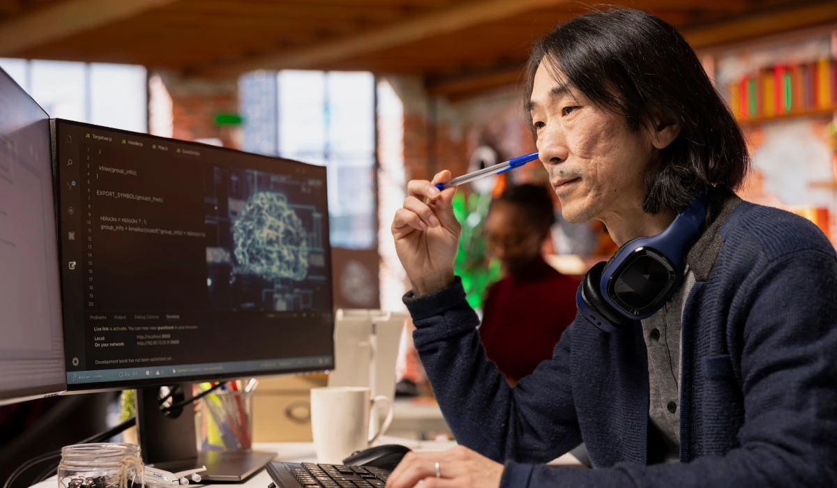 A man sitting at a desk, focused on his computer, with a pen in hand ready to take notes.