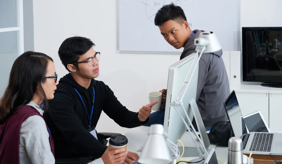 A diverse team of three people focused on a computer in an office, engaged in teamwork and discussion.