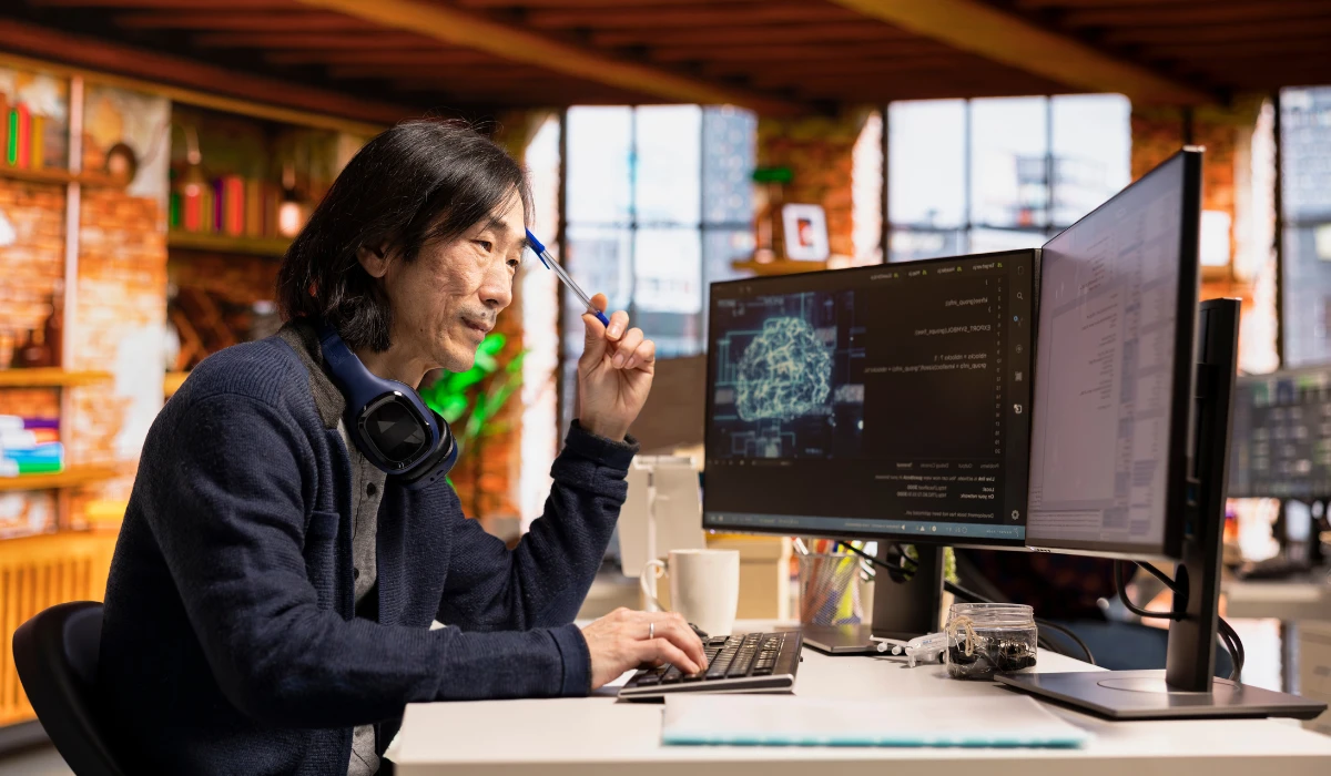 A man sitting at a desk, working on a computer with a monitor in front of him.