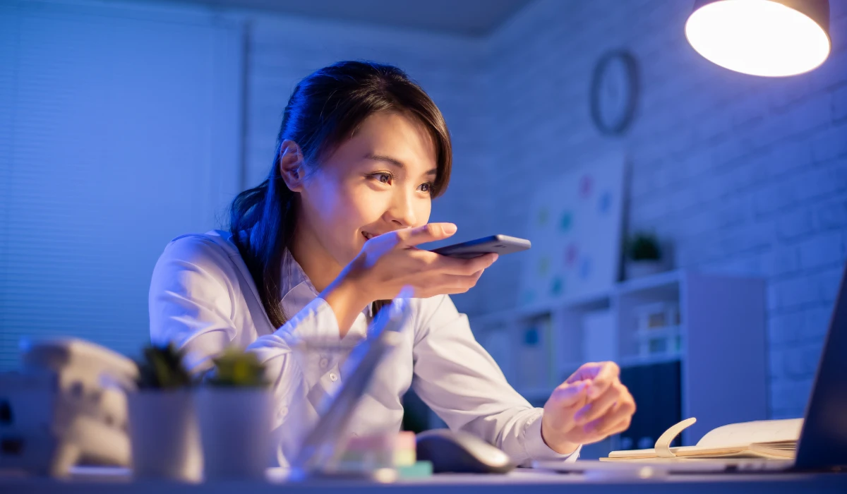 A woman sitting at her desk, focused on her cell phone while working.