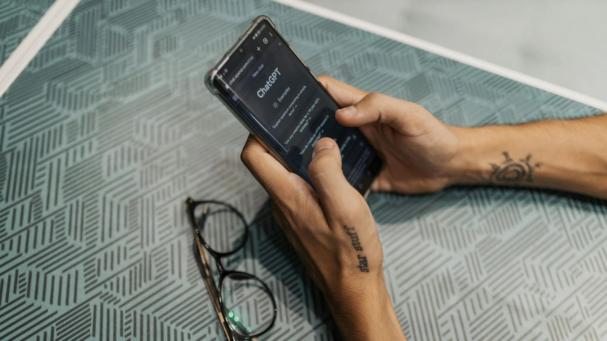 A person sitting at a table, focused on using a smartphone in their hands.