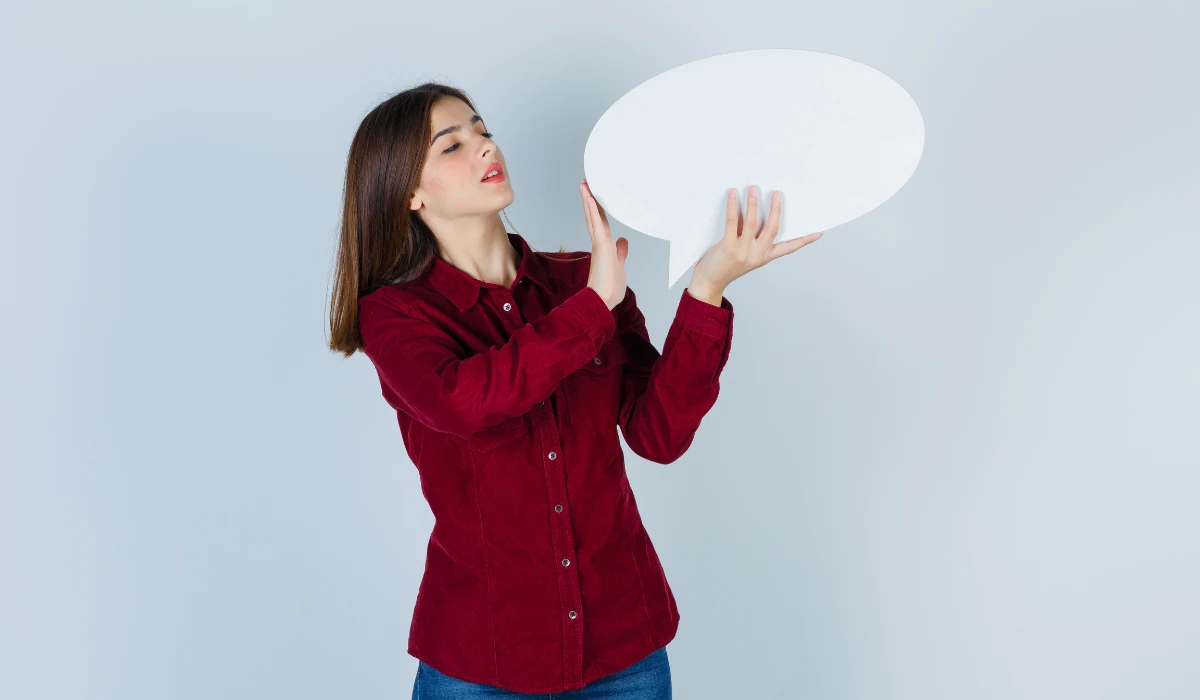 Woman smiling and holding a white speech bubble, suggesting communication or sharing ideas.