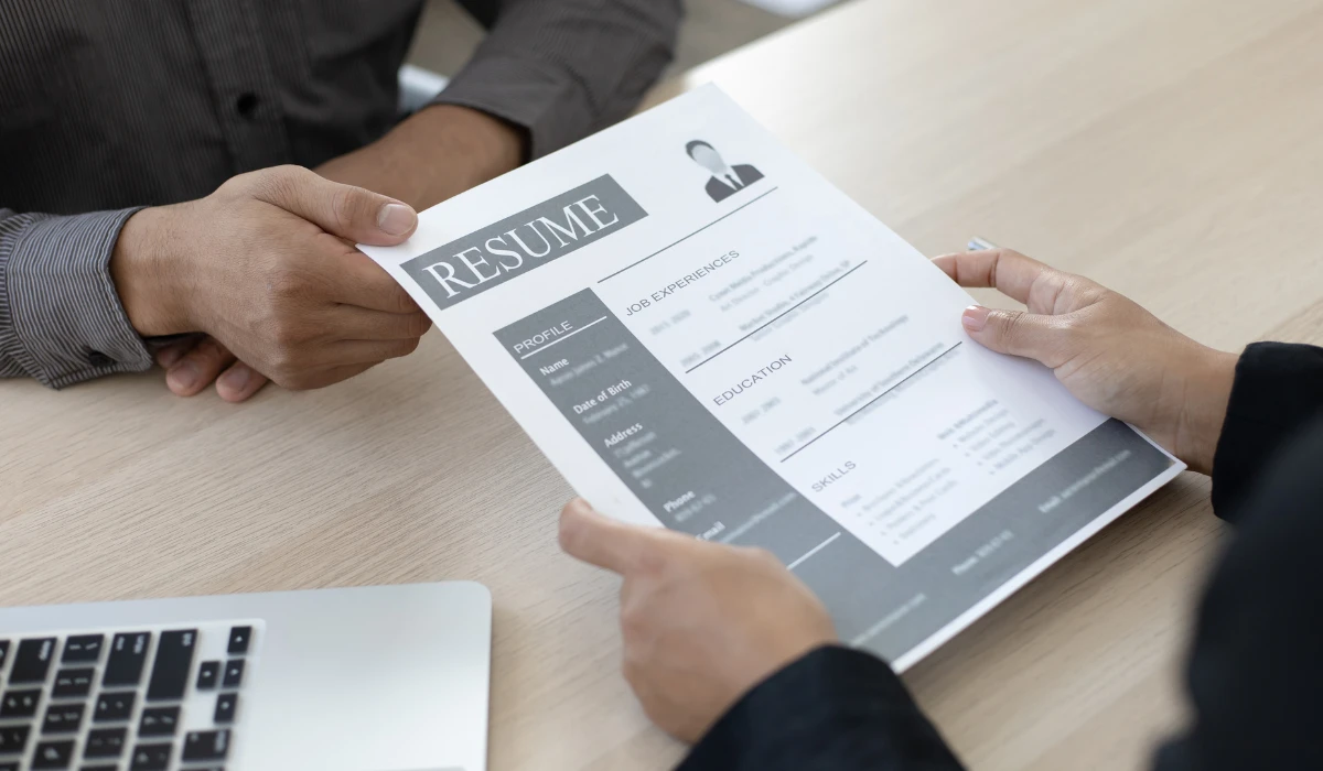 A person presents a resume on a table while another person listens attentively during a discussion.
