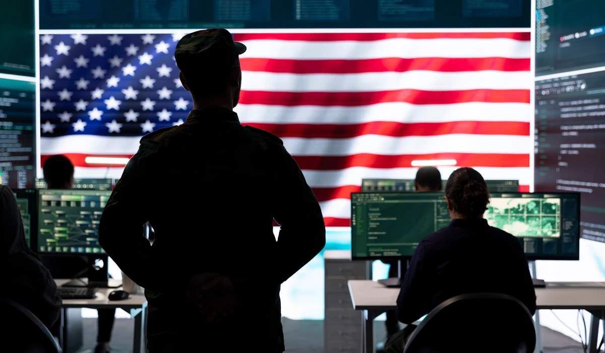 A man in uniform intently observes a computer screen, focused on his work.