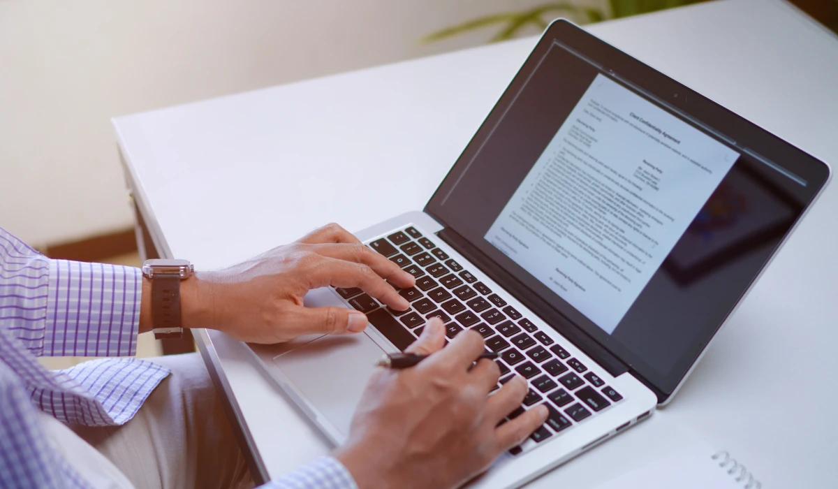 A person focused on typing on a laptop, with hands on the keyboard and a bright screen in front of them.
