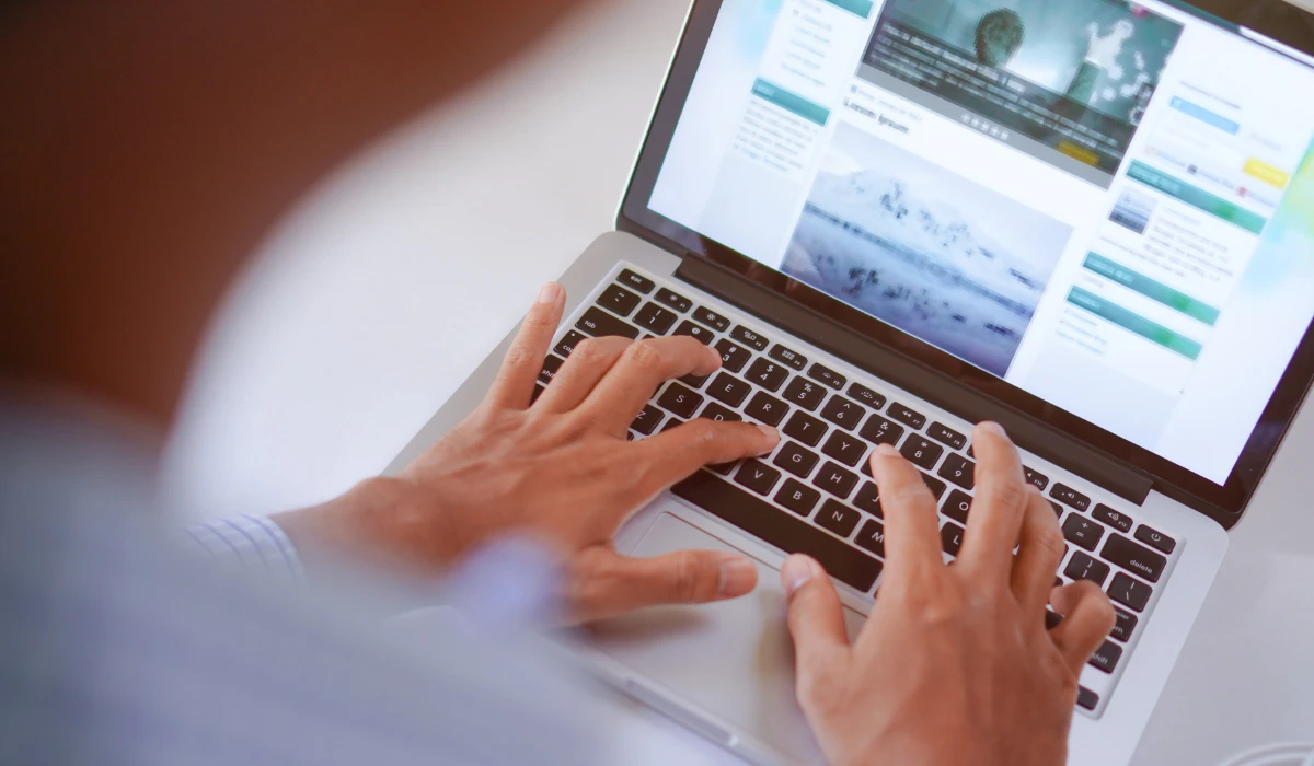 A person engaged in typing on a laptop, with a cozy workspace visible in the background.