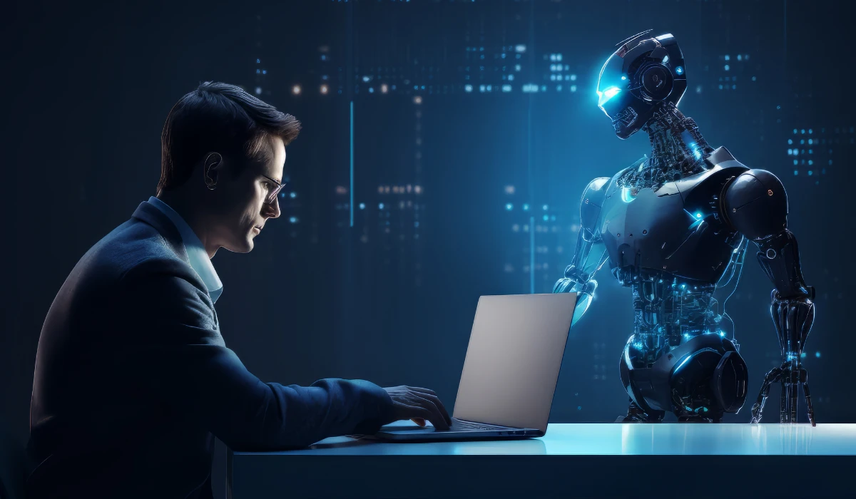 A man in a suit works on a laptop while a friendly robot observes him from the side.