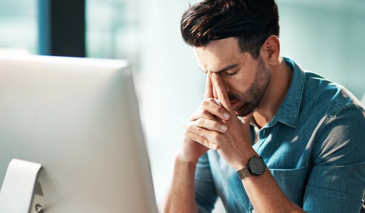 A man at a desk, with his hand on his face, appearing deep in thought or pondering something.