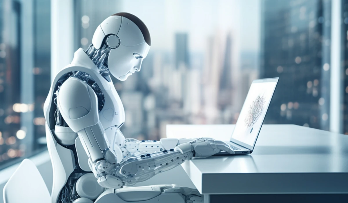 A friendly robot sitting at a desk, focused on a laptop, surrounded by office supplies.